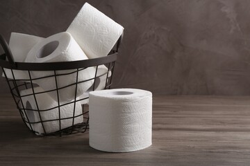 Soft toilet paper rolls in metal basket on wooden table, closeup. Space for text