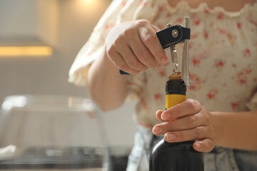 Woman opening wine bottle with corkscrew on blurred background, closeup. Space for text