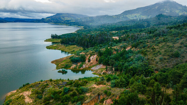 Aerial view of serene Embalse de Tomin&eacute;, Guatavita, Cundinamarca, surrounded by lush greenery and mountains under a cloudy sky