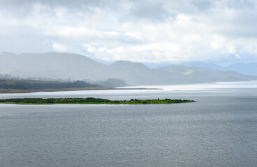 Scenic view of the serene Embalse de Tominé in Guatavita, Cundinamarca, showcasing lush greenery amidst tranquil waters under a cloudy sky