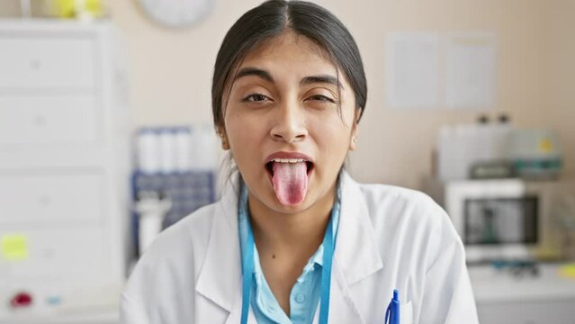 Hilarious snapshot, happy young indian woman, tongue sticking out, pulling a funny face in labcoat at laboratory work