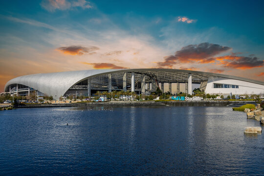 A beautiful spring landscape at SoFi Stadium with lush green palm trees and plants, a lake with birds swimming and powerful clouds at sunset in Inglewood California USA