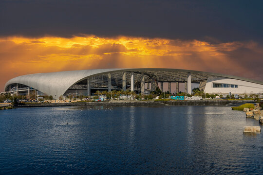 A beautiful spring landscape at SoFi Stadium with lush green palm trees and plants, a lake with birds swimming and powerful clouds at sunset in Inglewood California USA