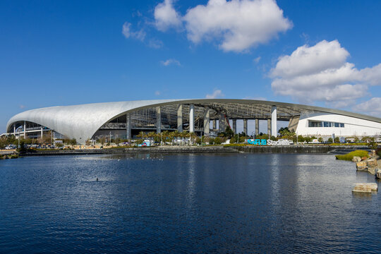 A beautiful spring landscape at SoFi Stadium with lush green palm trees and plants, a lake with birds swimming, blue sky and clouds in Inglewood California USA