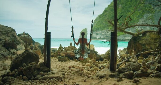 Woman on swing facing the sea at Bali's secluded Tembeling beach and Forest, ideal for tranquil travel. Pristine Ocean waves.