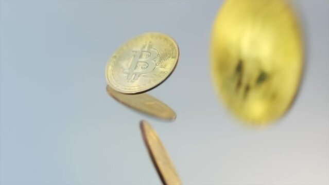 Shimmering golden Bitcoin coins fall in slow motion on gray mirror table close-up. A lot of cryptocurrency BTS Bitcoin. Tracking shot.