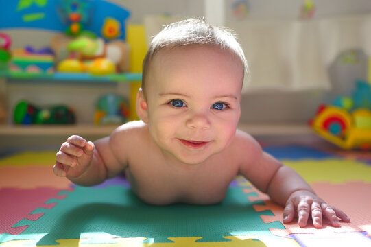 Adorable smiling cute funny happy infant baby in diaper crawling and playing on the floor on a developing foam puzzle play mat with toys in nursery room. Healthy child concept. Baby goods packaging