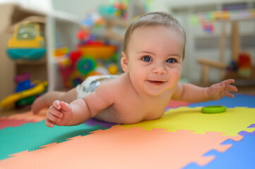 Fototapeta na wymiar Adorable smiling cute funny happy infant baby in diaper crawling and playing on the floor on a developing foam puzzle play mat with toys in nursery room. Healthy child concept. Baby goods packaging