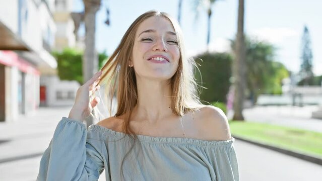 A cheerful young woman smiles brightly on a sunny urban street, exuding a casual, happy vibe in a shoulder-baring top.