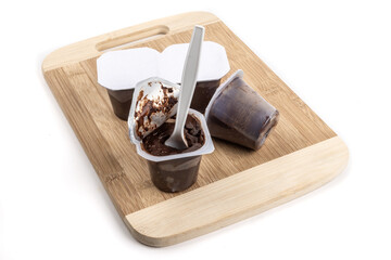 Chocolate grocery store pudding cups with a plastic spoon in one cup on a wooden board