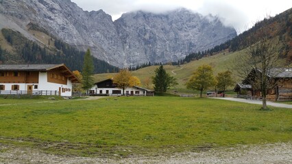 green grassy field and houses stretches beneath majestic towering mountain range, painting a...