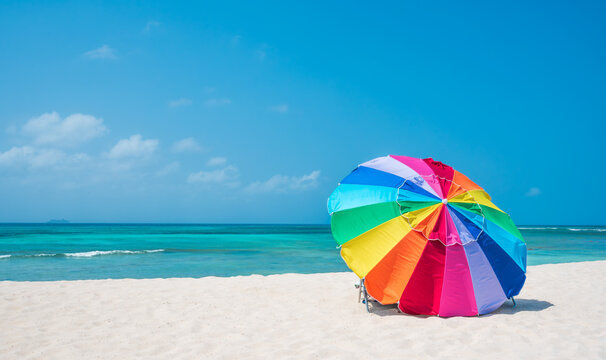 Multicolour vibrant rainbow beach umbrella on a beautiful hot and clear sunny day, with cruise ship on the horizon, turquoise water, Arashi Beach, Aruba, Caribbean Sea. Photo taken in February 2024.