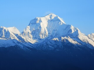 A majestic snow-covered mountain shines brightly under a clear blue sky