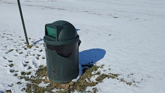 Trash can waste receptacle outside in snow on sunny winter day