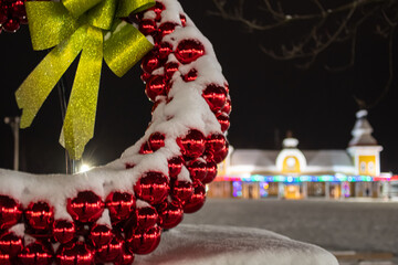 red Christmas ball wreath with gold ribbon in North Conway NH blurred lighted train station in...