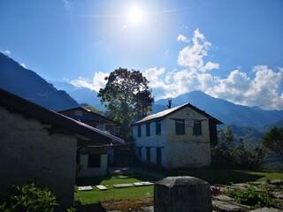 In the mountainous setting, the radiant sun casts its bright rays upon a house, illuminating it beautifully.