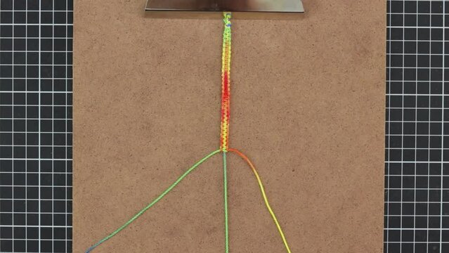 Hands weaving rainbow-patterned macrame bracelet, with colorful threads, Timelapse