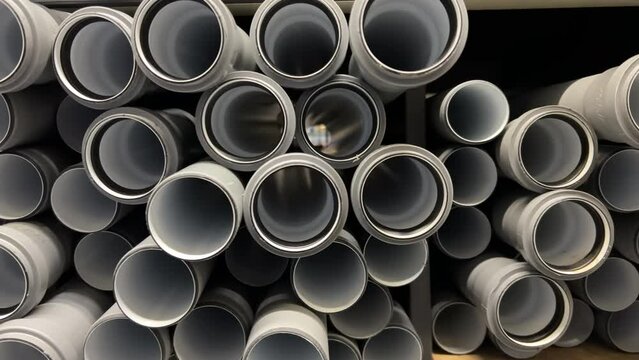Close-up front view of a rows of plastic water pipes stacked on a shelf in a hardware store. The pipes are of different sizes, diameters. They are made of high-quality plastic