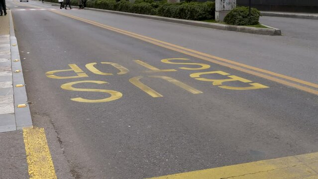 Pedestrians crossing bus lane with BUS STOP sign printed on an asphalted road with yellow paint.