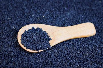 Black Cumin seeds in wooden spoon on Black Cumin background.