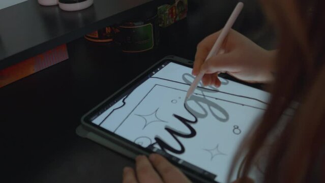 a female tattoo artist with long red hair drawing a design for a tattoo on an tablet as she traces each cursive letter