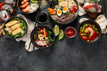 Traditional Asian food table. Spring roll, rice, shrimp, sushi, vegetables, meat on dark background