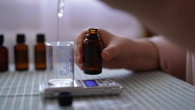 Closeup side view of unrecognizable female artisan craftperson dropping essential oil into glass bottle using pipette. Process of making handmade natural scented candle at workshop, slow motion.