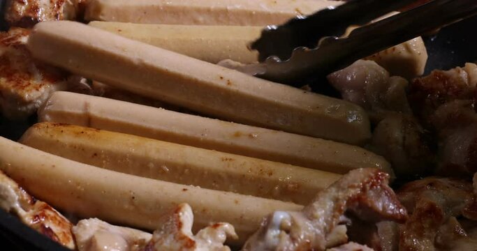 Frying skinless small chicken fillet pieces sausage bangers in lightly coated oil thyme herb non stick pan cooking sizzling dark golden brown putting taking serving rolling stir