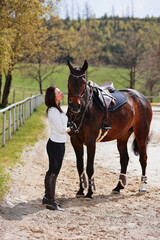 Young Frtau rider with brown long hair in portrait with her horse on the riding arena.