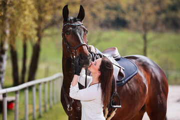 Young Frtau rider with brown long hair in portrait with her horse on the riding arena.