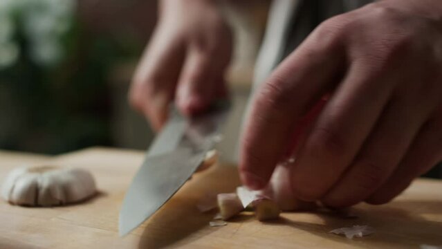 Closeup of unrecognizable male chef smashing fresh garlic with knife on wooden cutting board