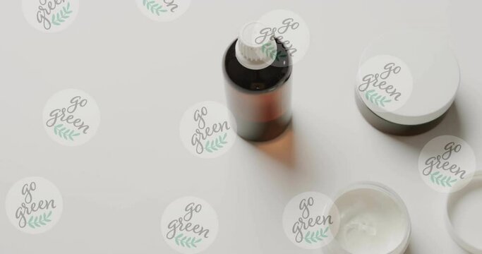 Animation of go green text and logos, over beauty cream jars and essential oil on white background