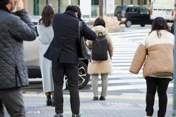 冬の朝の通勤時間の都市の交差点の横断歩道で信号待ちの人々の姿