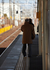 冬の朝の電車の駅のホームで電車待ちのシニア男性の姿