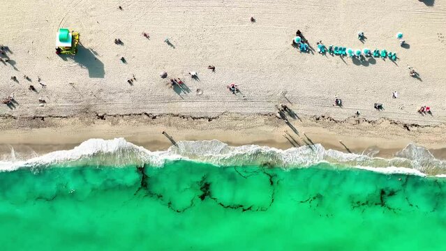 The shore of South Beach Miami with small waves crashing on shore with some umbrellas and people on the beach.
