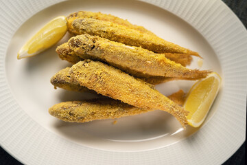 Red mullet fried in breadcrumbs served on a white plate with lemon slices, close-up.