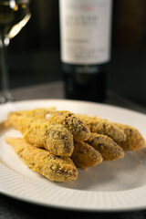 Mullet fish fried in breadcrumbs served on a white plate with wine in the background. Restaurant menu concept.