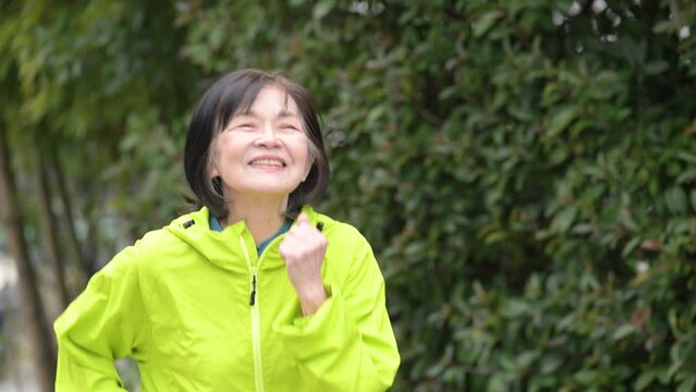Close-up of an elderly woman's upper body walking and running in a park in fresh green Slow motion picture of an image of an active senior