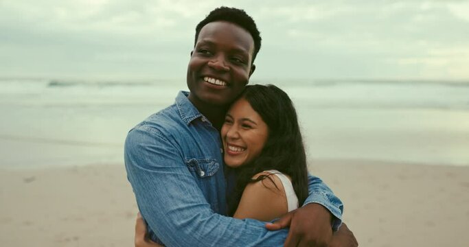 Happy, love and couple hugging on beach for romantic, anniversary or love date on vacation. Smile, travel and interracial young man and woman embracing by ocean on holiday or weekend trip together.