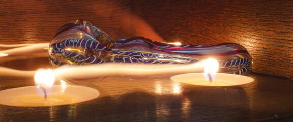 Illuminated candles placed on a table in front of a dichroic glass pipe