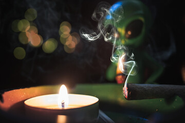 Small glowing candle with cigarette smoke and an alien silhouette in the backdrop
