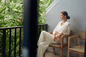 Smiling Woman on Tropical Balcony, Enjoying a Relaxing Vacation in Trendy Sunglasses This captivating image features a young woman standing on a sunny balcony, overlooking a lush tropical landscape