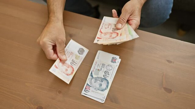 A man handles singaporean currency indoors, showcasing finance and home scenarios.