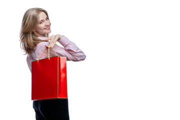 Happy young girl with a red gift bag in her hands. Cute smiling blonde girl wearing a pink shirt and blue trousers. Surprises and gifts during the holidays. Isolated on white background. 