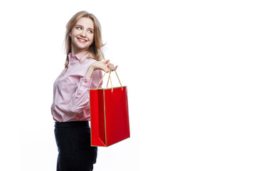 Happy young girl with a red gift bag in her hands. Cute smiling blonde girl wearing a pink shirt and blue trousers. Surprises and gifts during the holidays. Isolated on white background.