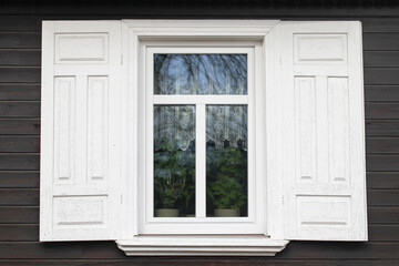Fototapeta premium Wooden rustic window in cottage house. Abandoned forsaken wooden home. Rusty architecture. Podlasie region in Poland vintage wall. Peeling paint decorative exterior shutter. Dark wood home wall facade
