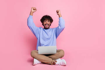 Photo of cheerful glad man sit floor celebrate win video game betting esport fists hands up isolated on pink color background