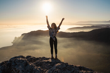 Fototapeta na wymiar Happy girl on mountain peak with raised arms looking at beautiful mountain valley at sunset in summer. Landscape with sporty young woman. Travel and tourism. Hiking. Travel concept 
