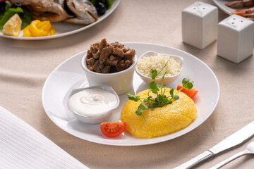 Delicious polenta with cheese, stew meat and sour cream on white plate serving on table. Traditional romanian healthy food