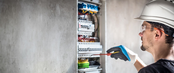 Male electrician working in switchboard with electrical connection cable.